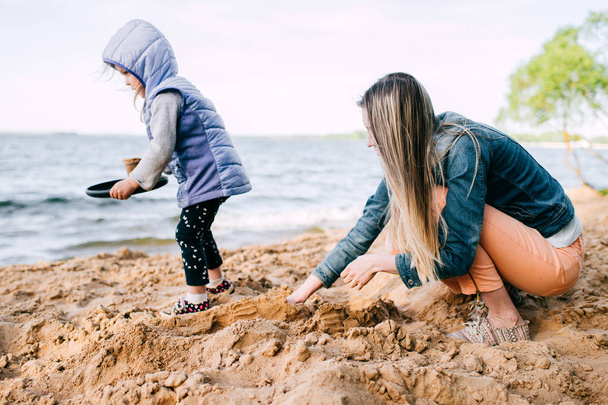 young mother and little daughter building sand castle on beach - 写真・画像