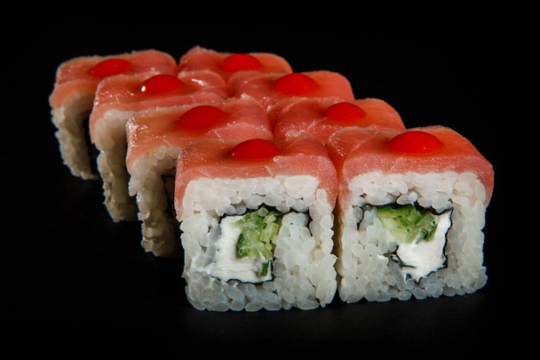 Closeup philadelphia broodje sushi met tonijn, komkommer en Philadelphia roomkaas versierd met rode saus geserveerd op zwarte achtergrond - Foto, afbeelding