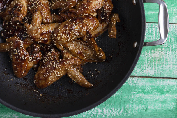 sweet salt chicken wings into cauldron with sesame on wooden table, top view - Photo, Image