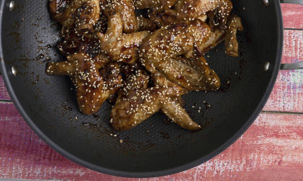 chicken wings with teriyaki sauce into cauldron on wooden table, closeup - Photo, Image