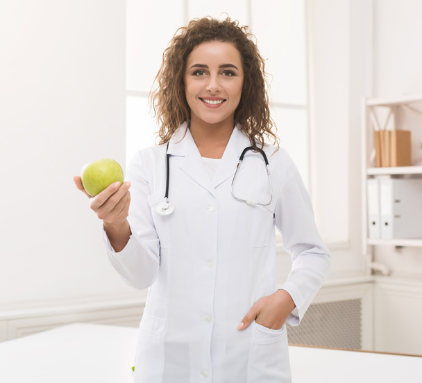 Ravitsemusterapeutti nainen tarjoaa vihreää omenaa kameran edessä
 - Valokuva, kuva