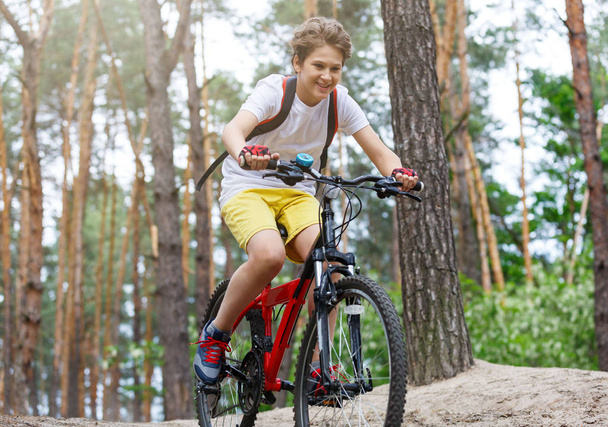 Kind tiener in wit t-shirt en gele broek op fiets rijden in bos bij lente of zomer. Gelukkig lachend jongen fietsen buitenshuis. Actieve lifestyle, hobby - Foto, afbeelding