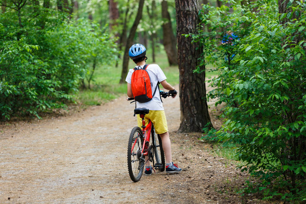 Adolescente criança em camiseta branca e calções amarelos em passeio de bicicleta na floresta na primavera ou no verão. Happy sorrindo Boy andar de bicicleta ao ar livre. Estilo de vida ativo, hobby
 - Foto, Imagem