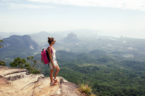 Jeune voyageuse avec sac à dos debout au sommet d'une montagne et profitant de la vue
 - Photo, image