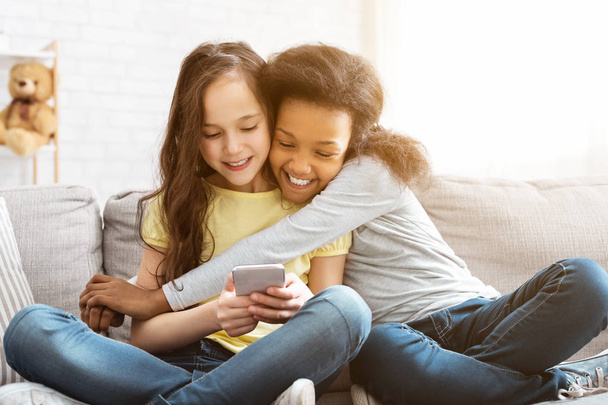 Happy little girls using smartphone and hugging at home - Foto, afbeelding