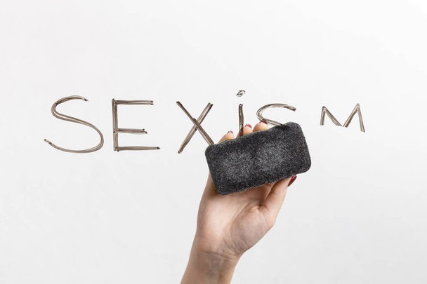 Sexism is written on glass and hand with sponge - Foto, afbeelding
