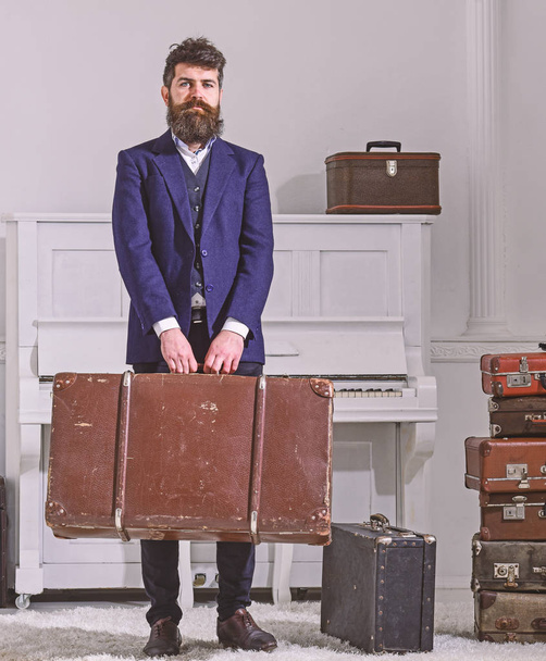 Baggage and travelling concept. Macho stylish on strict face stands and carries big vintage suitcase. Man, traveller with beard and mustache with baggage, luxury white interior background - Foto, Imagem