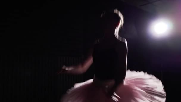 Young and graceful ballerina dancing on her pointe ballet shoes in spotlight on black background in studio.. Woman shows classic ballet pas wearing tutu and pointe shoes. Slow motion. - Video