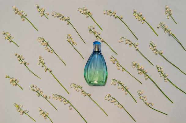 Bottle of perfume and lily of the valley flowers on light pastel background. Perfumery, fragrance, cosmetic concept. Spring or summer composition. Flat lay, top view - Fotó, kép