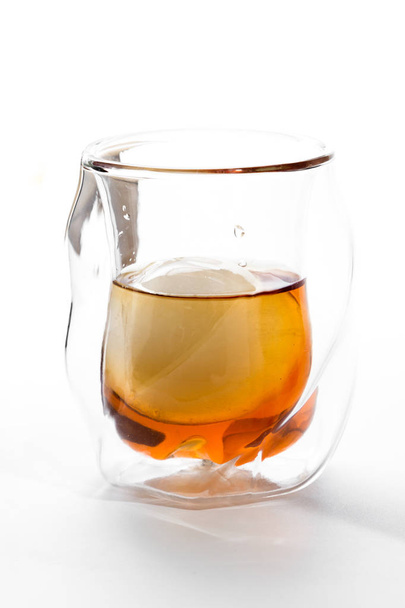 Bourbon served in a double walled whisky glass served with an ice sphere over a white background - Foto, Imagem