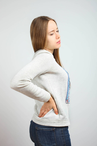 Beautiful sad caucasian girl with back pain is standing against neutral background. Concept disease. - Photo, Image