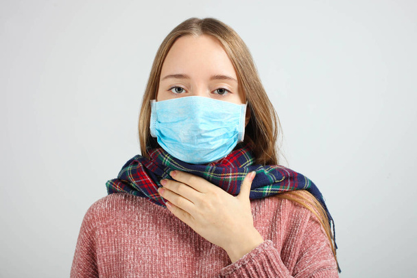Ένα άρρωστο κορίτσι σε μπλε ιατρική μάσκα σε γκρι φόντο. Ιός, γρίπη. Έννοια υγείας. - Φωτογραφία, εικόνα