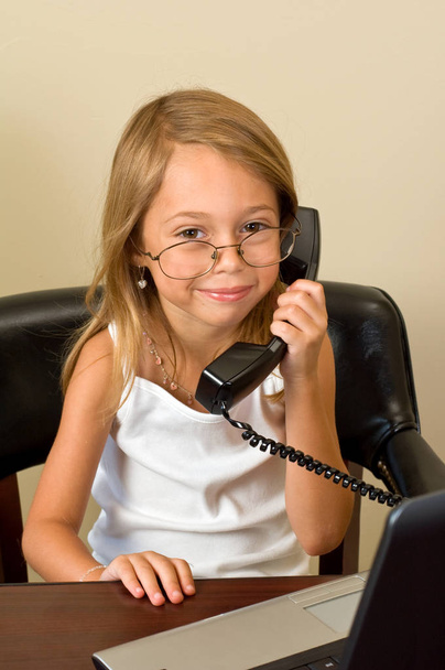 Młoda dziewczyna o 6 udaje się zajęty w jej notebooka podczas noszenia okularów za duży dla jej głowy, rozmowy na telefon. - Zdjęcie, obraz