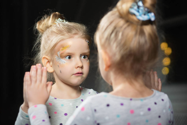 маленька дівчинка з барвистим обличчям дивиться на дзеркало
 - Фото, зображення
