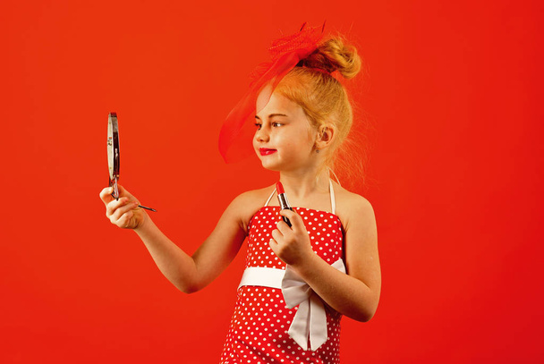 Little girl hold lipstick and mirror. Fashion and beauty, pinup style, childhood. Makeup retro look and hairdresser. Child girl in stylish dress, makeup. Retro girl fashion with cosmetics, beauty. - Photo, Image