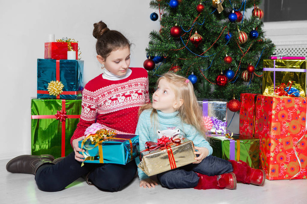 κορίτσια με δώρα που κάθονται κοντά στο γιορτινό χριστουγεννιάτικο δέντρο στο studio - Φωτογραφία, εικόνα