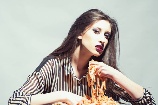 Beauty model with makeup and long brunette hair have dinner. Sexy woman eat spaghetti with hands. Woman eat pasta dish with tomato ketchup. Hungry girl have italian food meal. Food, diet and cuisine - Fotografie, Obrázek