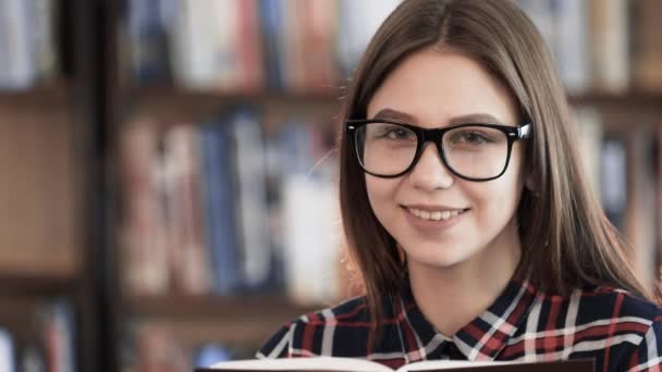 Schooling academical concept. Young female 20s successful persone read book in class room. Pretty teenager try to concentration for homework holding in hands educational literature and laugh to camera - Footage, Video