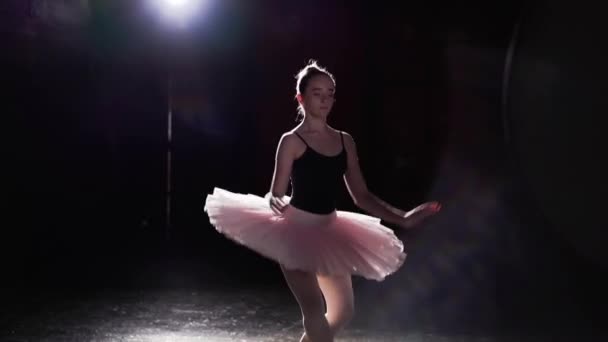 Graceful flexible girl dancing on her pointe ballet shoes in spotlight on black background in studio. Professional ballerina shows classic ballet pas wearing tutu and pointe shoes. - Metraje, vídeo