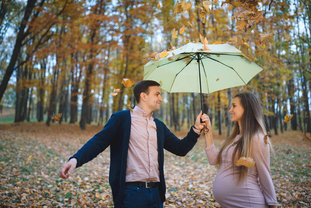 έγκυος γυναίκα στο φόρεμα και τρυφερός σύζυγος υπαίθρια στο πάρκο, άνθρωπος ομπρέλα εκμετάλλευση  - Φωτογραφία, εικόνα