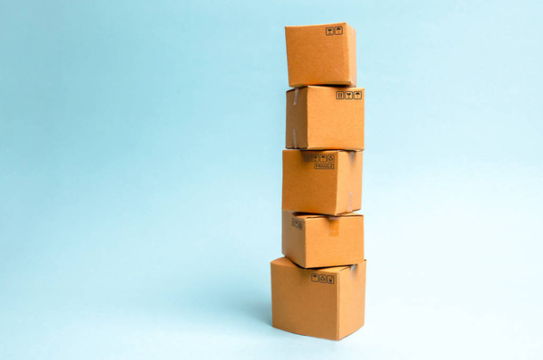 Torre de cajas de cartón sobre fondo azul. El concepto de movimiento y entrega de bienes y mercancías. Comercio y procesos de negocio, logística, distribución y ventas
. - Foto, imagen