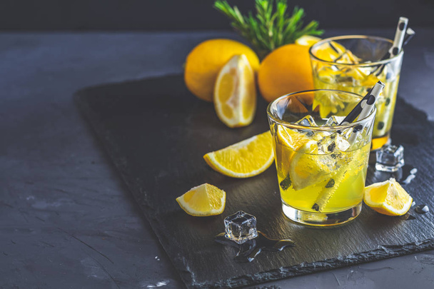 Sitruunaalkoholi juo cocktailia jäällä, sitruunalla ja rosmariinilla mustalla kivibetonipinnalla. Perinteinen italialainen sitruuna alkoholi juoda likööri limoncello
. - Valokuva, kuva