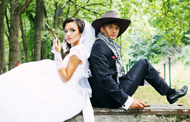  Beautiful bride and groom in a cowboy hat, they smoke - Foto, imagen