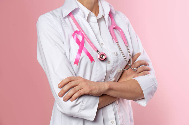 Female doctor with pink ribbon and stethoscope on color background, closeup. Breast cancer concept - Valokuva, kuva