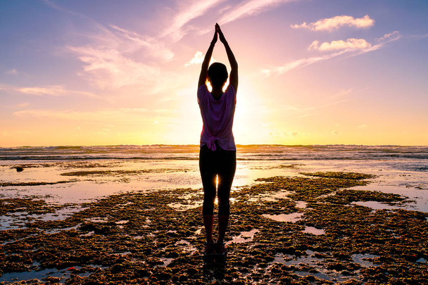 Joven mujer sana practicando yoga en la playa al atardecer. Mujer fuerte confianza bajo el atardecer en la playa. Silueta de mujer joven haciendo yoga en la playa
. - Foto, Imagen