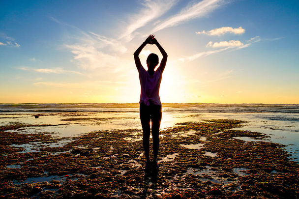 Jonge gezonde vrouw het beoefenen van yoga op het strand bij zonsondergang. Sterk vertrouwen vrouw onder de zonsondergang op zee. Silhouet van een jonge vrouw doet yoga op het strand. - Foto, afbeelding