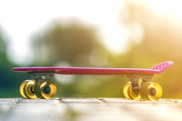 Close-up van kind kunststof roze skateboard geïsoleerd op bestrating tegen de achtergrond van de heldere witte en groene wazig bokeh. Sport, recreatie, plezier en speelt concept. - Foto, afbeelding
