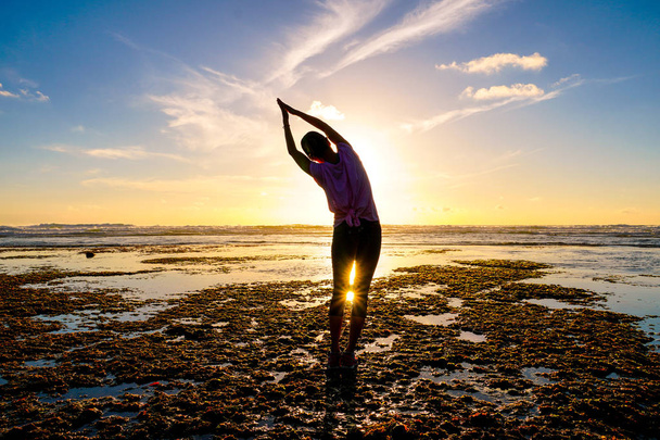 Молода здорова жінка практикує йогу на пляжі під час заходу сонця. Сильна впевненість жінка під час заходу сонця на узбережжі. Силует молодої жінки робить йогу на пляжі
. - Фото, зображення
