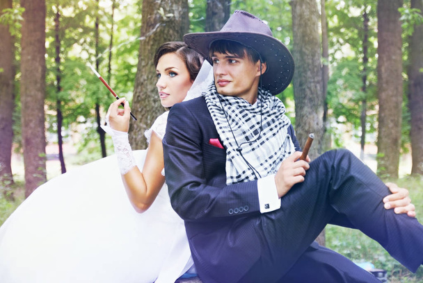  Beautiful bride and groom in a cowboy hat, they smoke - Photo, Image