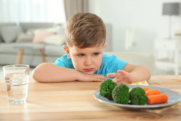 Cute African-American girl eating vegetable salad at table in room - Photo, image