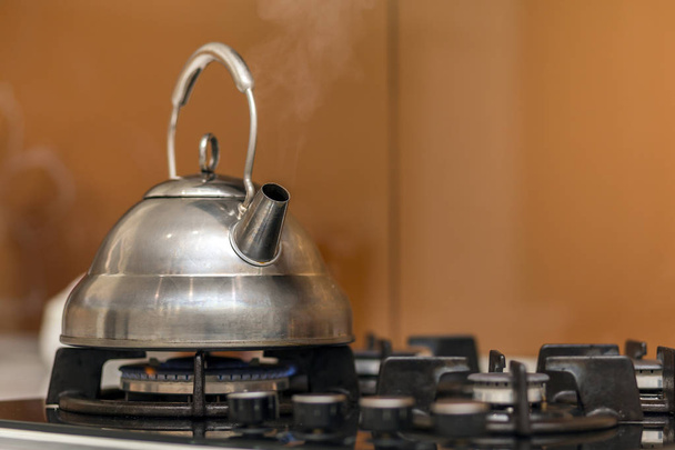 Блискучий чайник з нержавіючої сталі з киплячою водою на газовій плиті на жовтому фоні кухонного простору
. - Фото, зображення