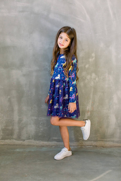 Fashion little girl child in blue dress on a grey background - Foto, imagen