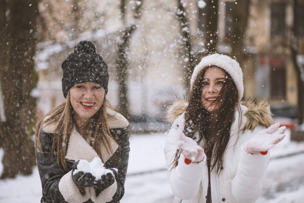 Young beautiful woman is enjoying the snow scattering it in the air. Winter outdoor activities, positive emotions, joy and happiness. - Zdjęcie, obraz