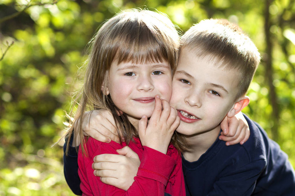 Δύο χαριτωμένο ξανθό αστεία ευτυχισμένη χαμογελαστά παιδιά αδέλφια, αγκαλιάζοντας αδελφή αδελφός αγόρι κορίτσι σε εξωτερικούς χώρους σε φωτεινό ηλιόλουστο bokeh πράσινο φόντο. Οικογενειακή σχέση, φιλία και αγάπη έννοια. - Φωτογραφία, εικόνα