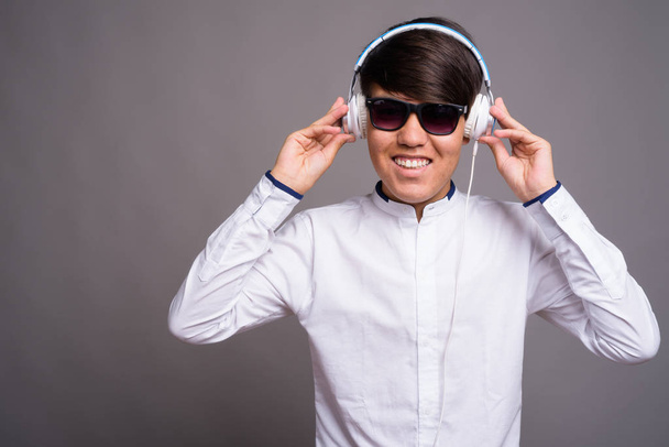 Young Asian teenage boy listening to music against gray backgrou - 写真・画像