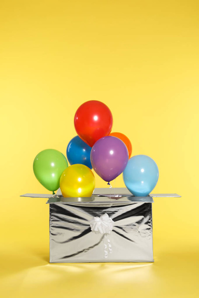 Gift box with bright air balloons on color background - Photo, Image