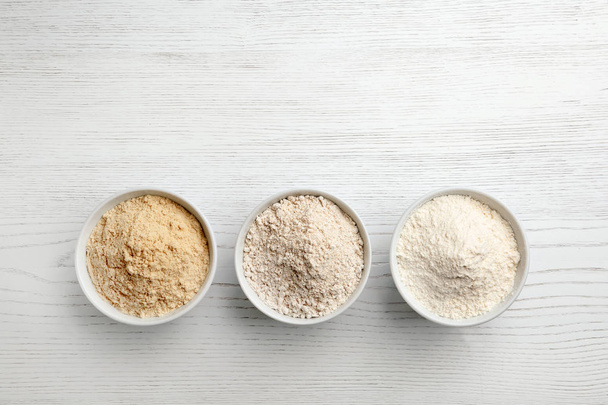 Bowls with different types of flour on white wooden background, top view. Space for text - 写真・画像