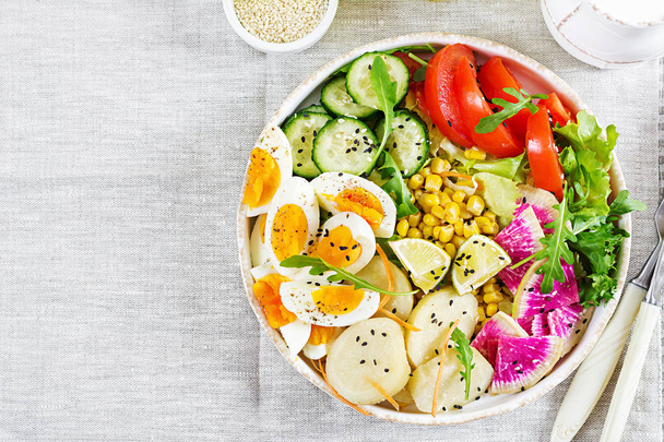Frisse salade met gekookte aardappel, komkommer, tomaten, watermeloen radijs, sla, rucola, maïs en gekookte eieren geserveerd op tafel - Foto, afbeelding
