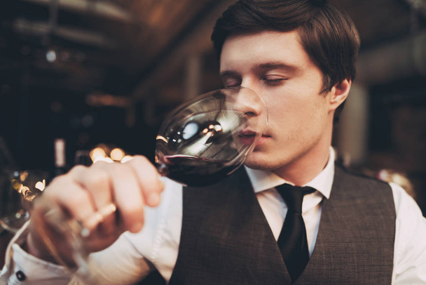 Close up. Young experienced sommelier tasting red wine, poured into glass, closing his eyes. - Foto, Bild