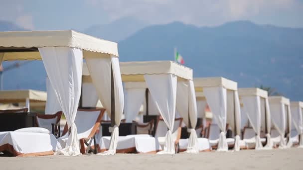 Akşam ışığında turkuaz bir denizin önünde tahta güneşlik yataklar. Forte dei Marmi 'deki ünlü İtalyan kumsalında güneşli yataklar. - Video, Çekim