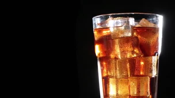 Cola z bąbelkami przelewa się do szklanki z lodem. Czarne tło - Materiał filmowy, wideo