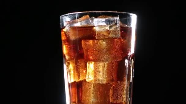 Cola con burbujas vertidas en un vaso de hielo. Fondo negro
 - Metraje, vídeo