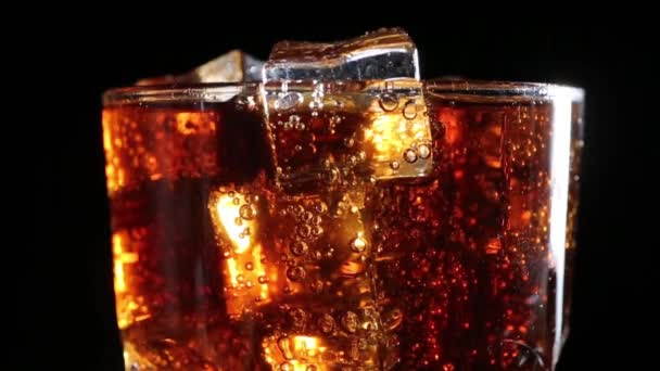 Cola with bubbles poured into a glass of ice.Black background - Záběry, video