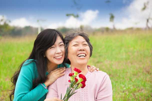 Lächelnde Tochter und ihre Mutter mit Nelkenblüte auf der Gra - Foto, Bild