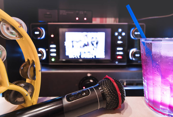 Zwarte microfoon in karaoke club, met afstandsbediening, meloen en aardbei frisdranken, gele tamboerijn en scherm voor zingen muziek op stadium partij. - Foto, afbeelding