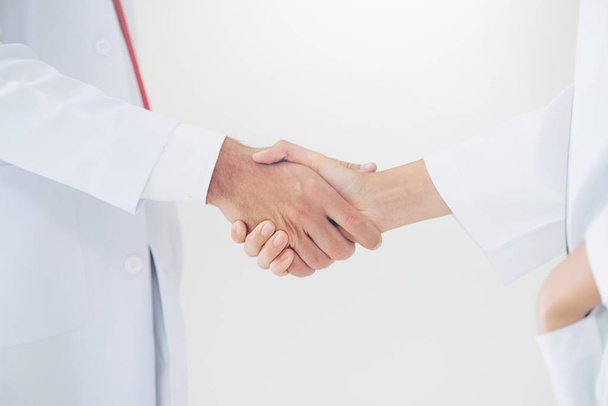 Doctor on white background giving handshake to another doctor showing success and teamwork of professional healthcare people. Close up at doctors hands. - Photo, Image
